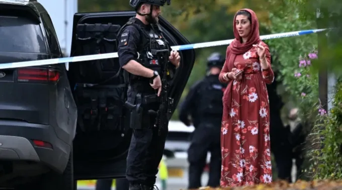 Policial armado conversa com membro da comunidade local do lado de fora da sinagoga da Congregação Hebraica de Heaton Park, em Crumpsall, norte de Manchester, Inglaterra em 2 de outubro de 2025 ?? 