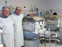 Erwin Bazan e o Padre Jordá ao lado da incubadora de Victoria no Hospital da Mulher em Santa Cruz. Crédito: Facebook Erwin Bazán