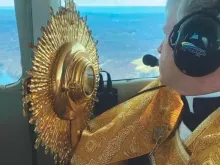 Pe. Brian Gannon voando em um helicóptero com Jesus Eucaristia. Créditos: St. Theresa Church