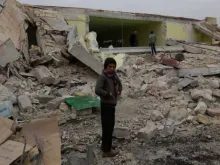 Menino diante das ruínas do prédio que era a sua escola em Aleppo (Síria).